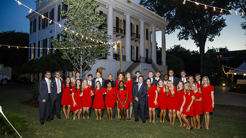 Larger group poses in front of the President's Mansion in the evening.